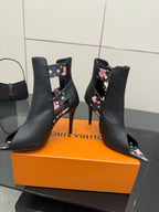 Pair of black ankle boots with floral side straps and gold-tone hardware.