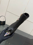 Single black ankle boot on hand, floral toe strap detail and slim heel.