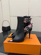 Black ankle boot with floral strap detail and tall stiletto heel, pointed toe.