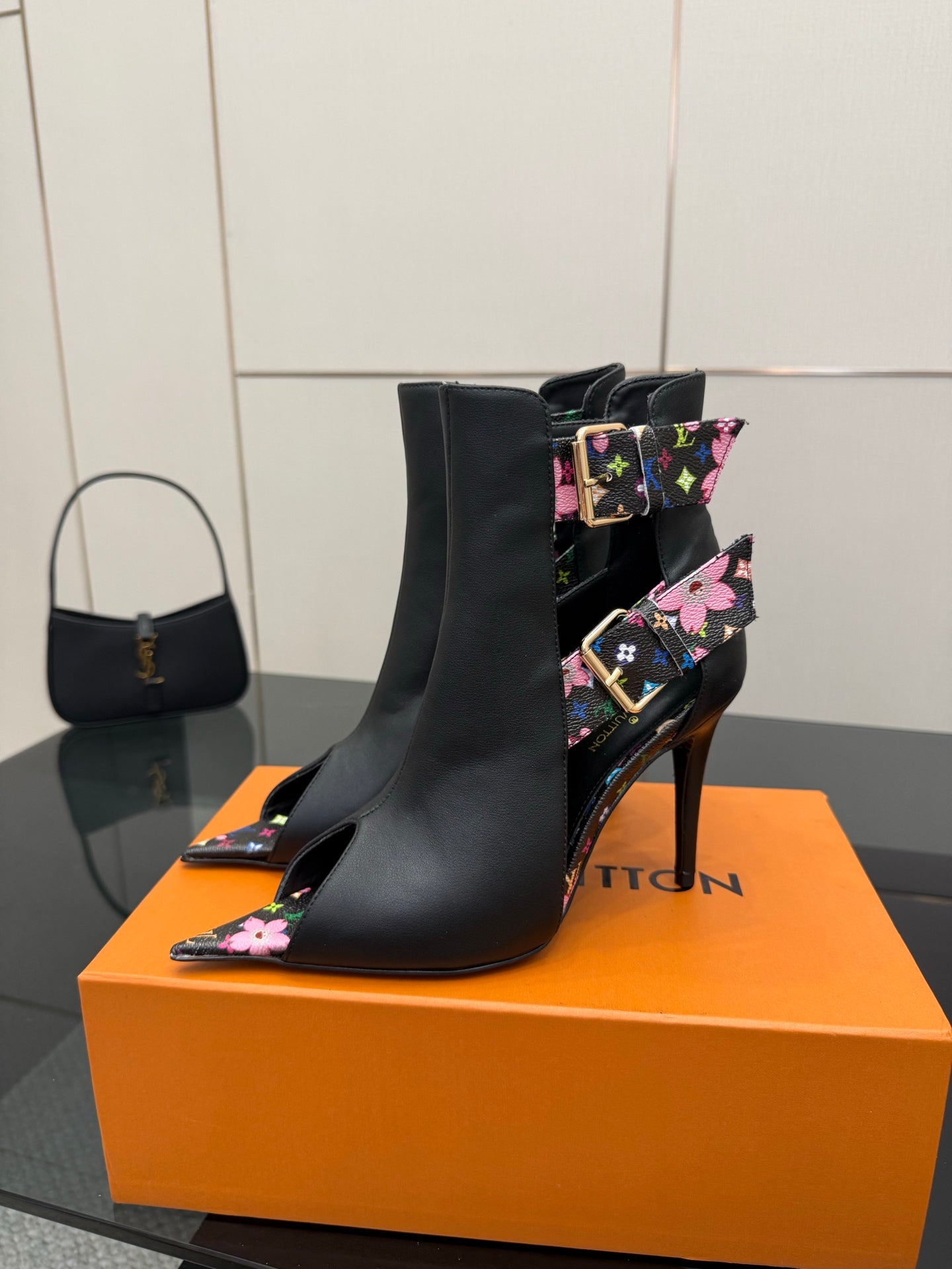 Black ankle boot with floral strap detail and tall stiletto heel, pointed toe.