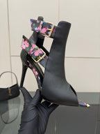 Close-up black ankle boot with floral strap, gold buckle, and pointed toe heel.