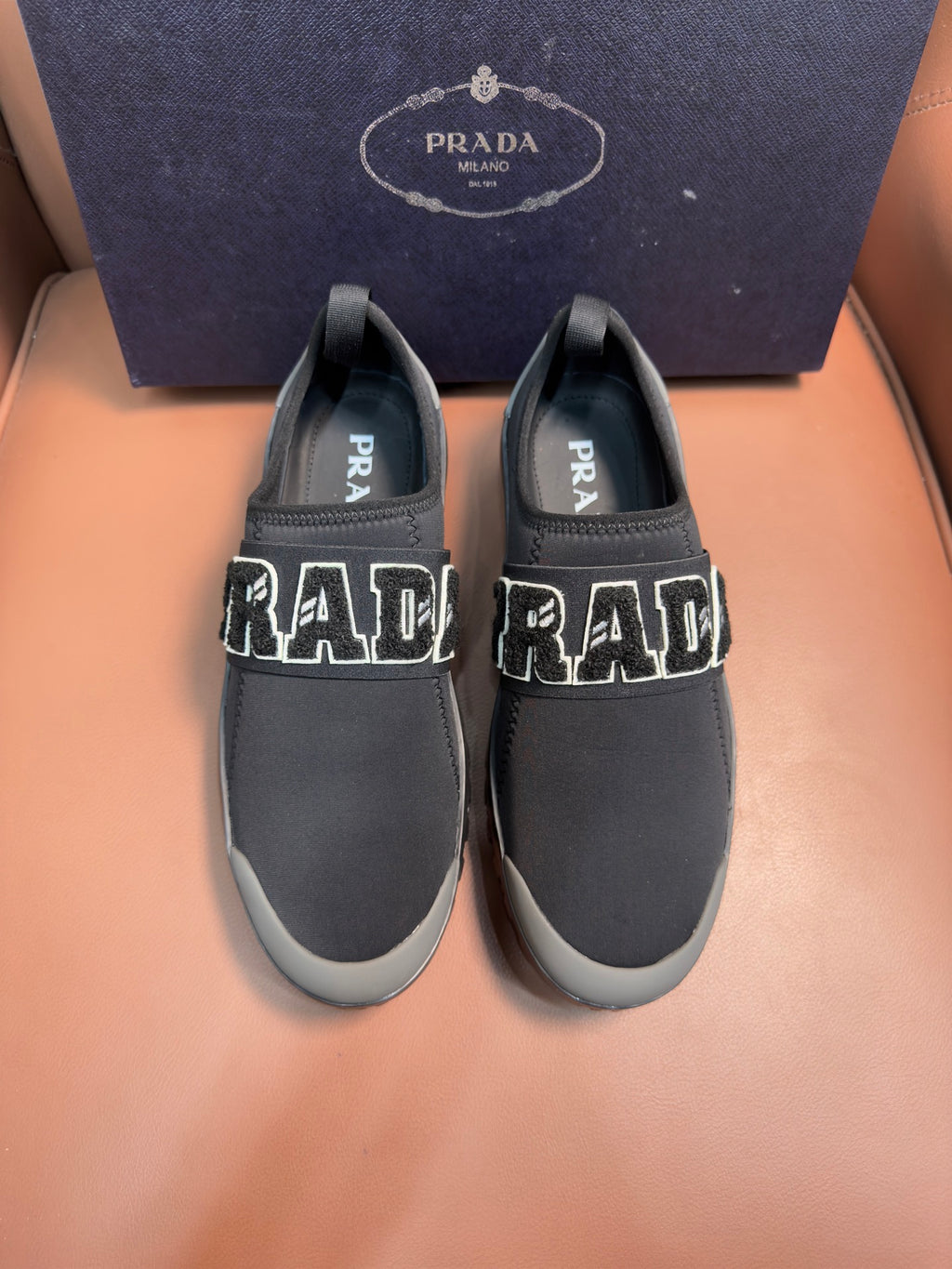 Prada unisex dark gray slip-on sneakers with large PRADA lettering on sides.