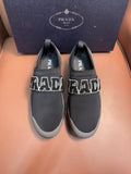Prada unisex dark gray slip-on sneakers with large PRADA lettering on sides.