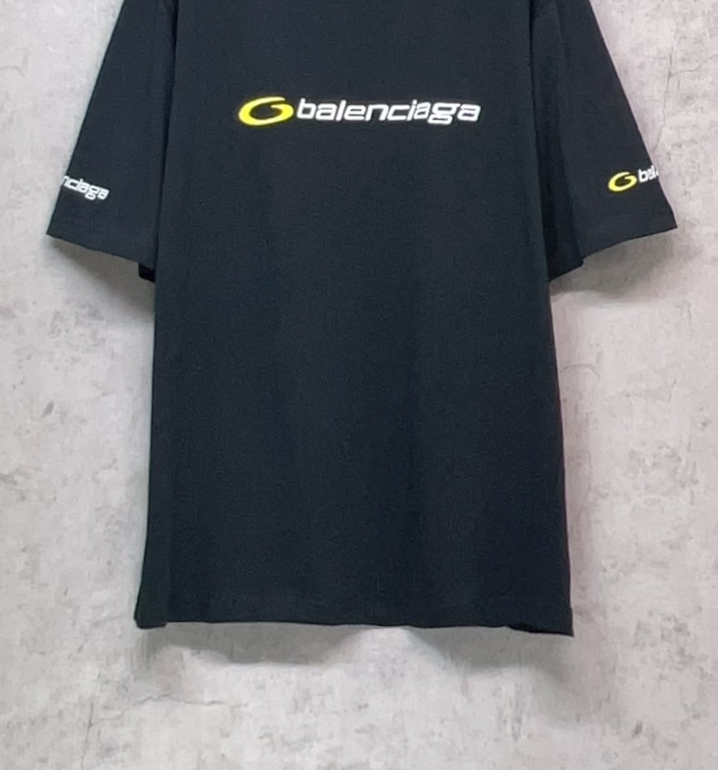 Dark T-shirt on hanger with yellow Balenciaga logo on the front and sleeve prints