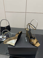 Gold open-toe heeled sandals on a black box, featuring silver ankle straps