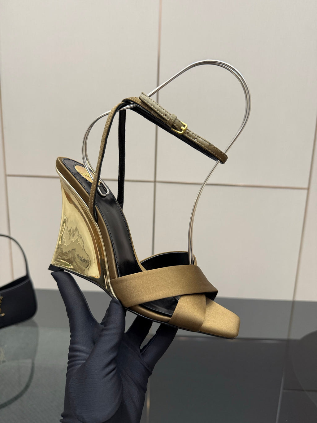 Gold and black open-toe heeled sandals held up, with silver ankle straps