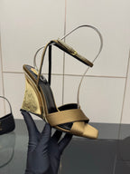 Gold and black open-toe heeled sandals held up, with silver ankle straps