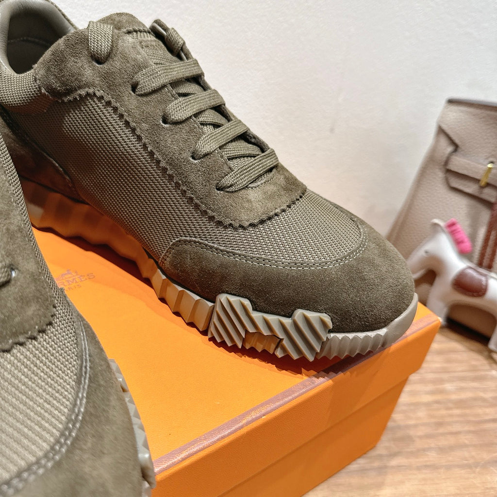 Hermes unisex sneaker close-up: olive canvas upper, lace-up, textured outsole and contrast stitching