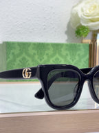 Gucci sunglasses close-up with dark navy frame, dark lenses, and gold GG logo