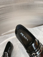 Black patent loafers with silver buckle strap, PRADA logo visible inside