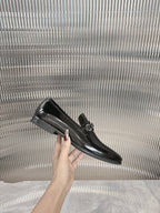 Black patent loafer held by hand, silver buckle strap detail