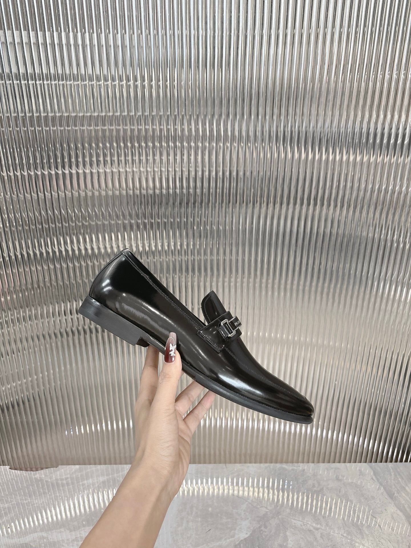 Black patent loafer held by hand, silver buckle strap detail