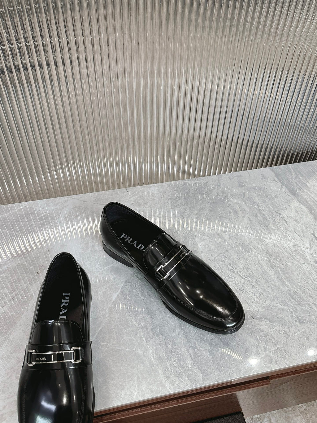 Black patent loafers with silver buckle strap and PRADA logo on upper