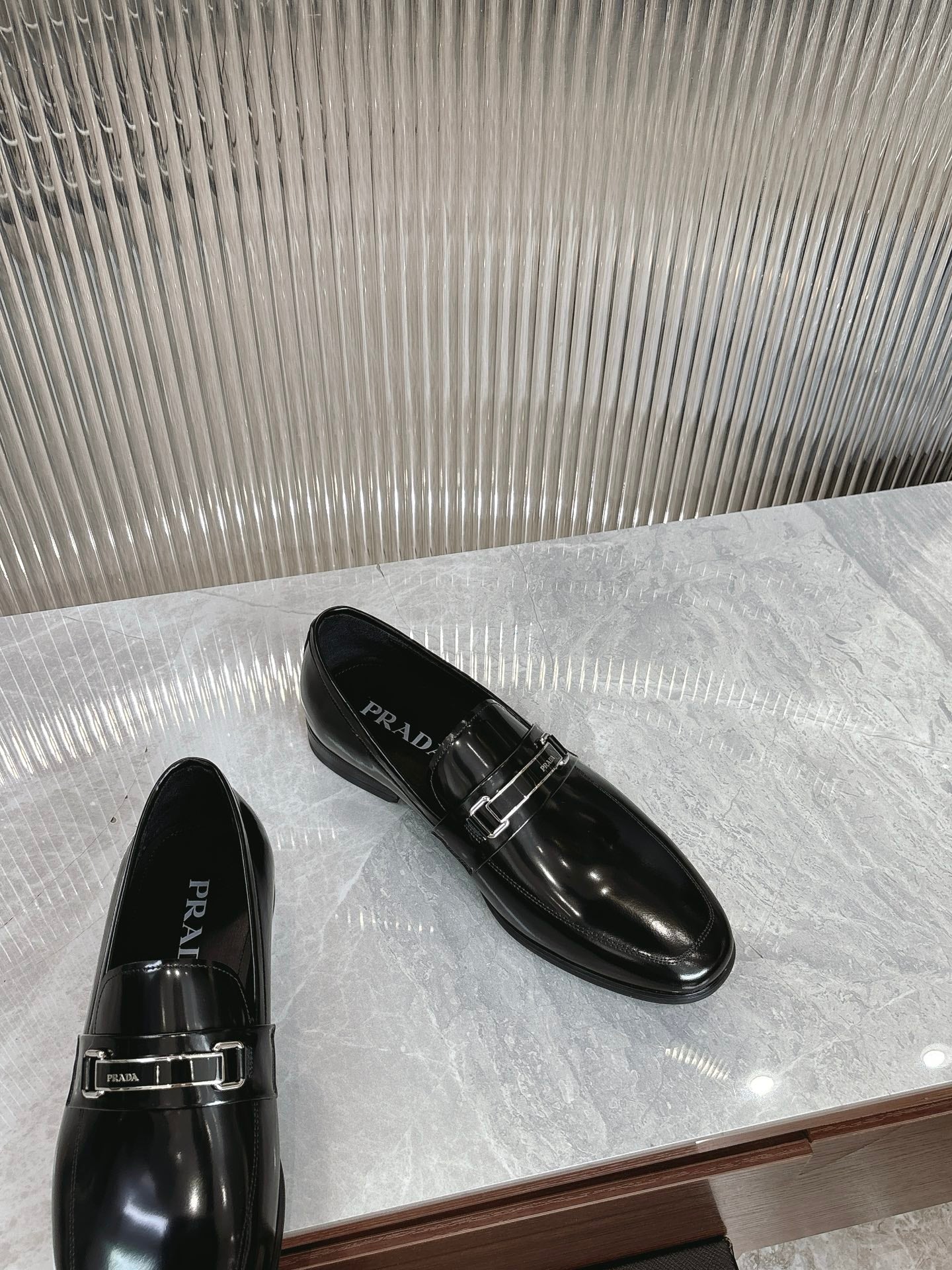 Black patent loafers with silver buckle strap and PRADA logo on upper