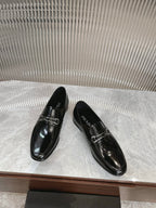Black patent leather loafers with silver buckle detail, two shoes angled