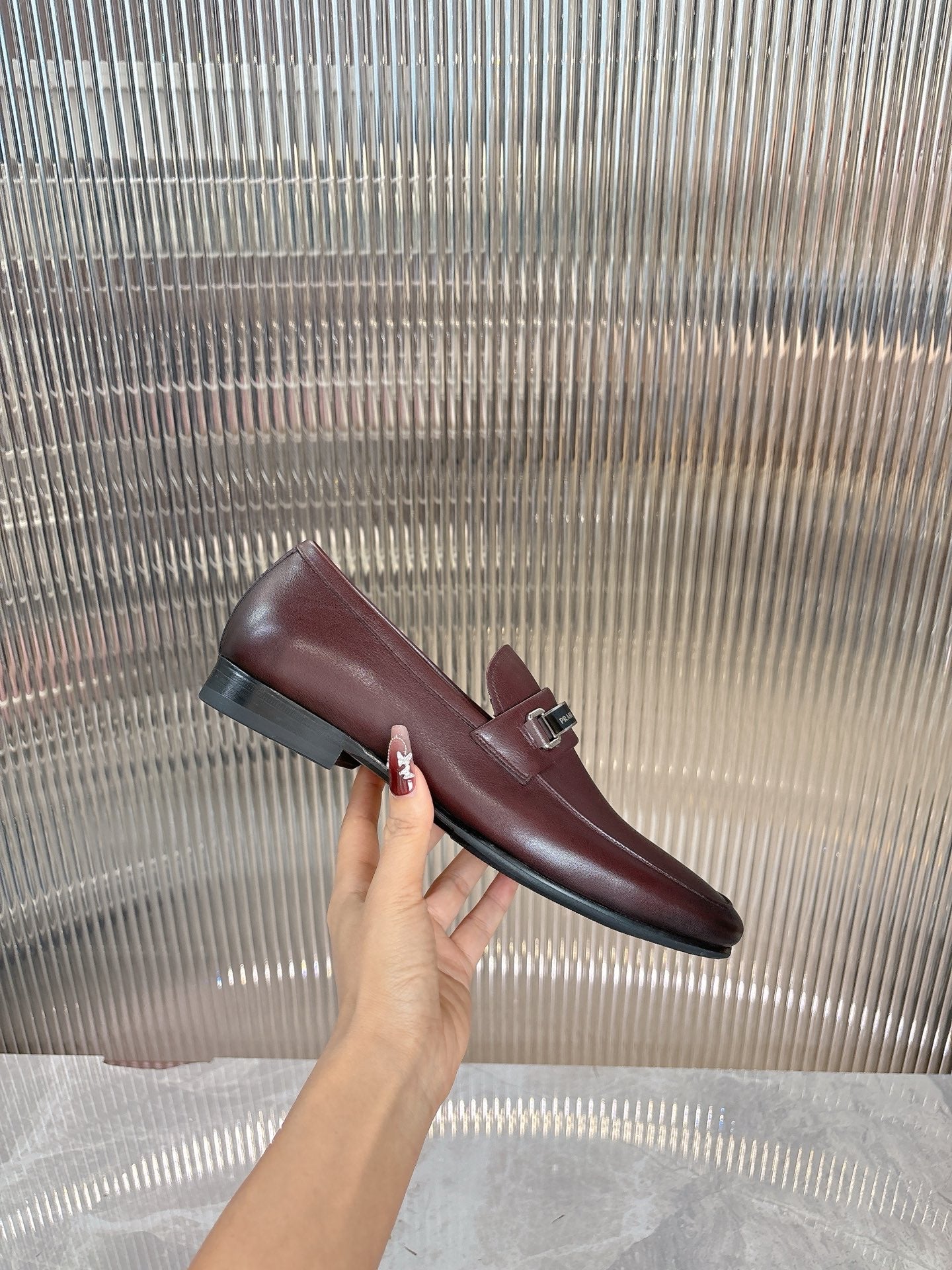 Prada unisex leather loafer, hand holding, dark burgundy slip-on with buckle