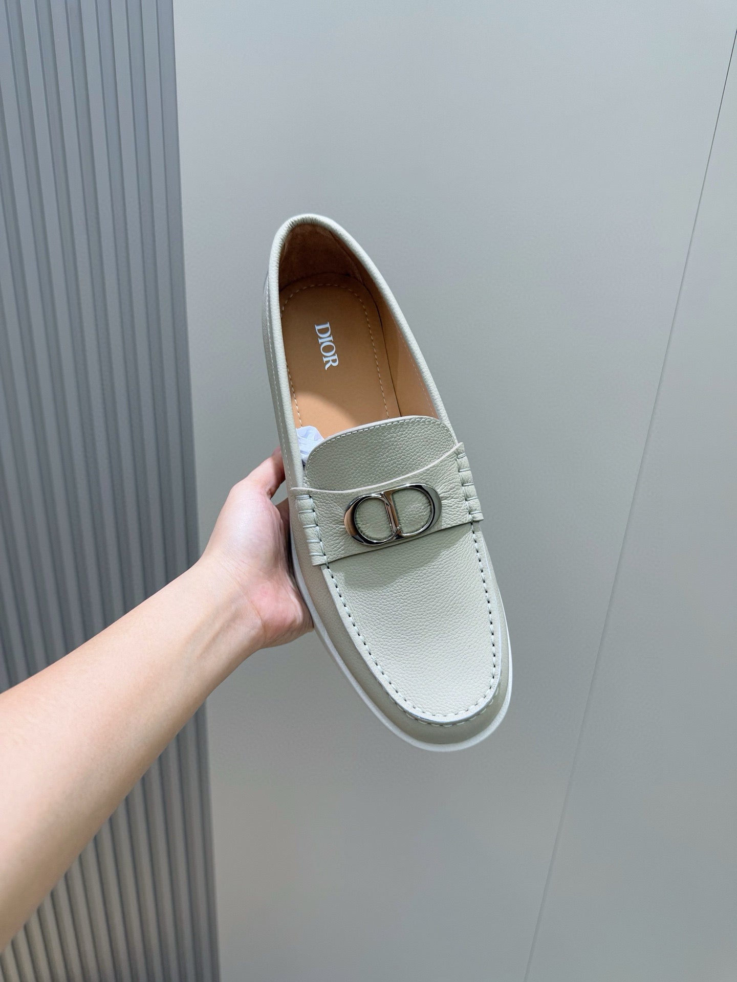Light beige loafer held up, silver-tone D buckle on the strap