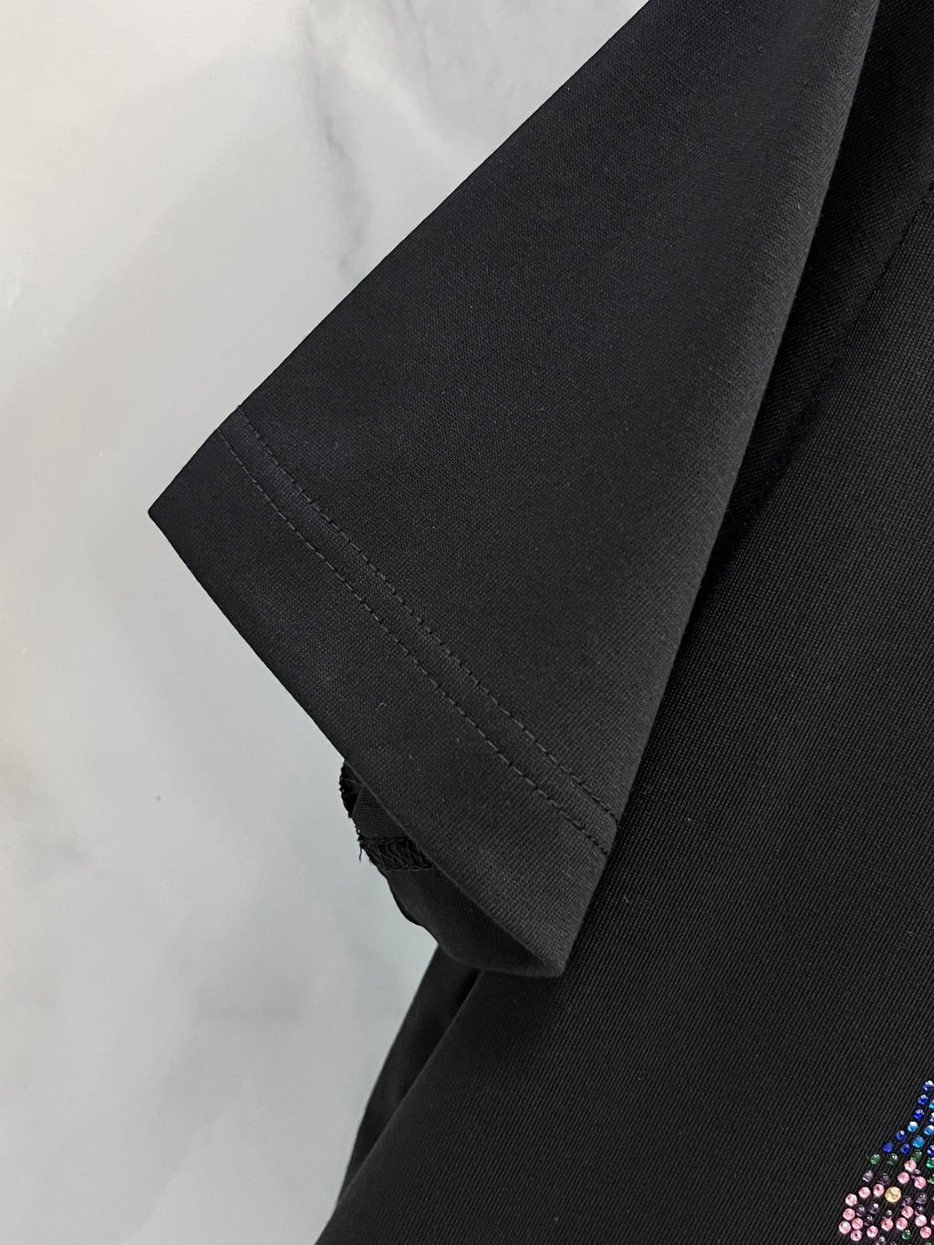Black T-shirt sleeve and hem detail on a hanger, no graphic visible on this area