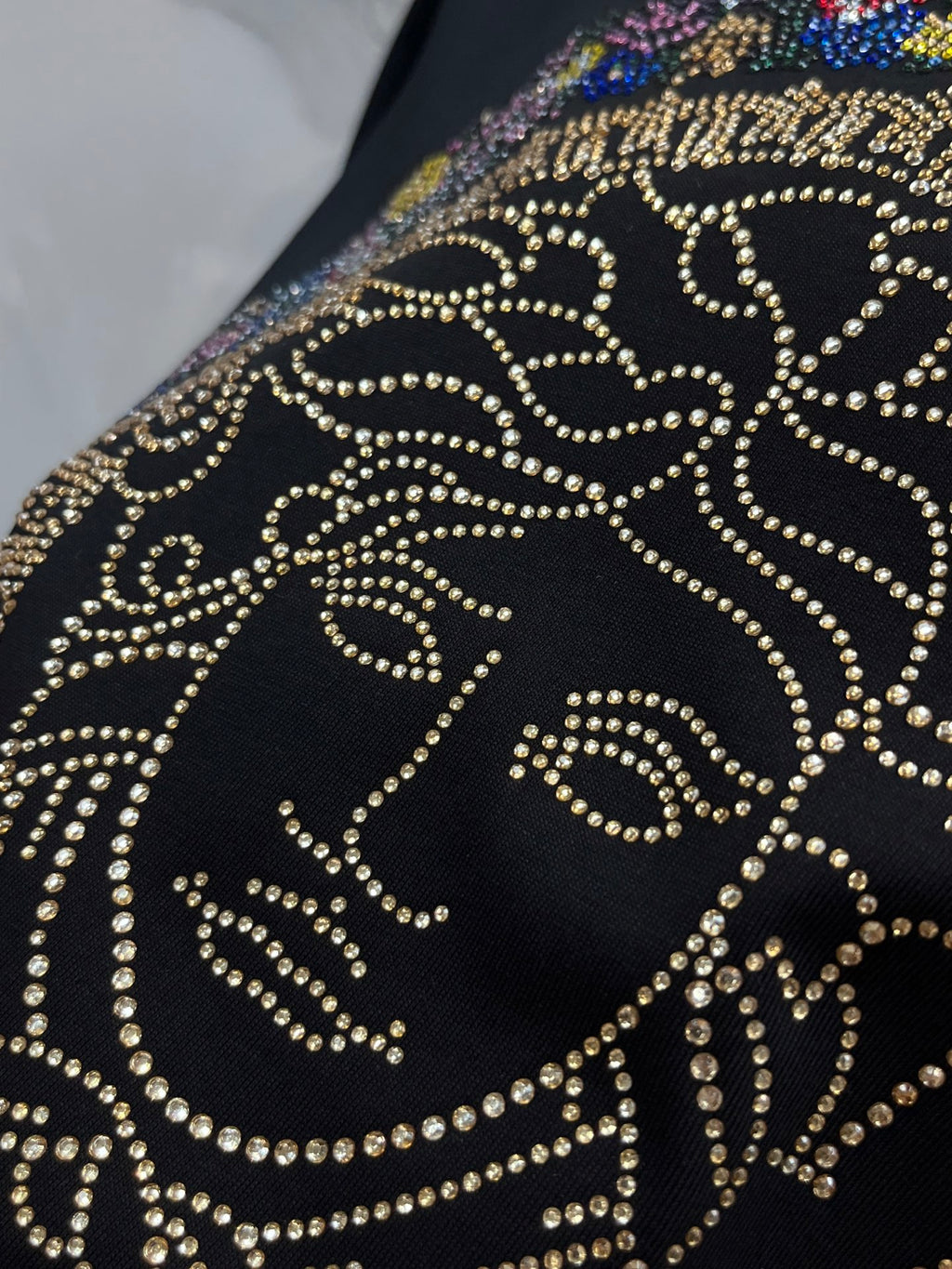 Rhinestone Medusa-style face graphic on a black T-shirt, close-up detail.