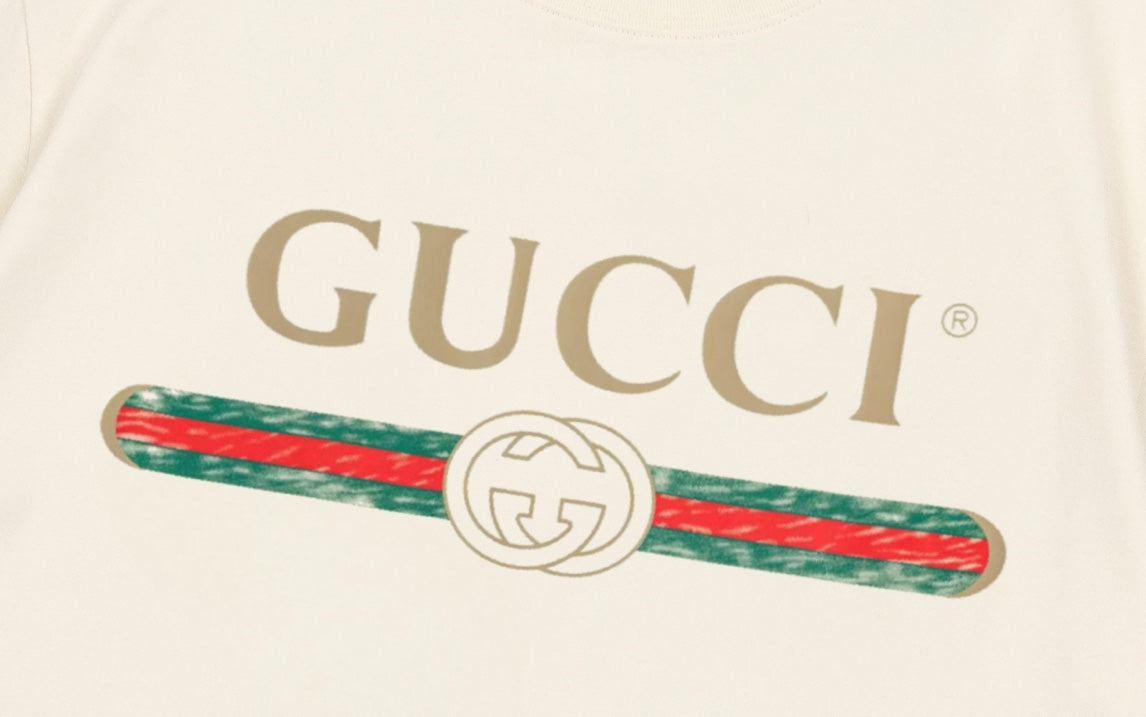 Cream Gucci T-shirt close-up: GUCCI text and striped emblem graphic