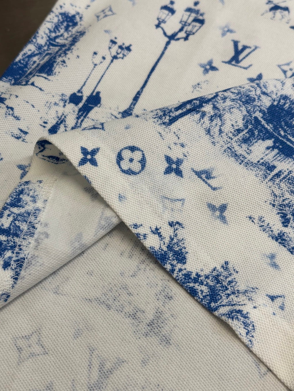 Collar and folded hem detail on off-white T-shirt with blue toile symbol print