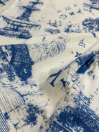 Close-up of off-white fabric with blue building and figure print, textured weave visible