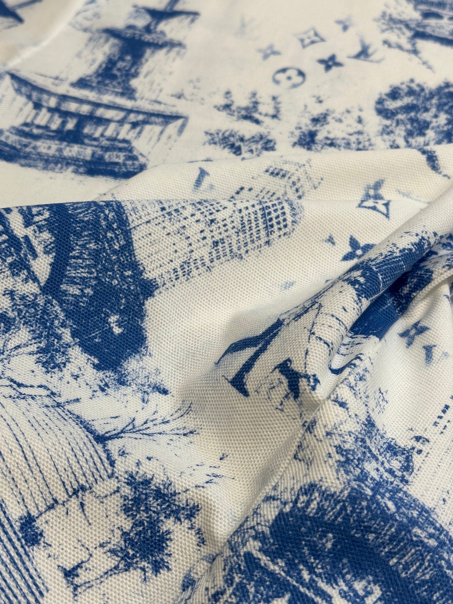 Close-up of off-white fabric with blue building and figure print, textured weave visible