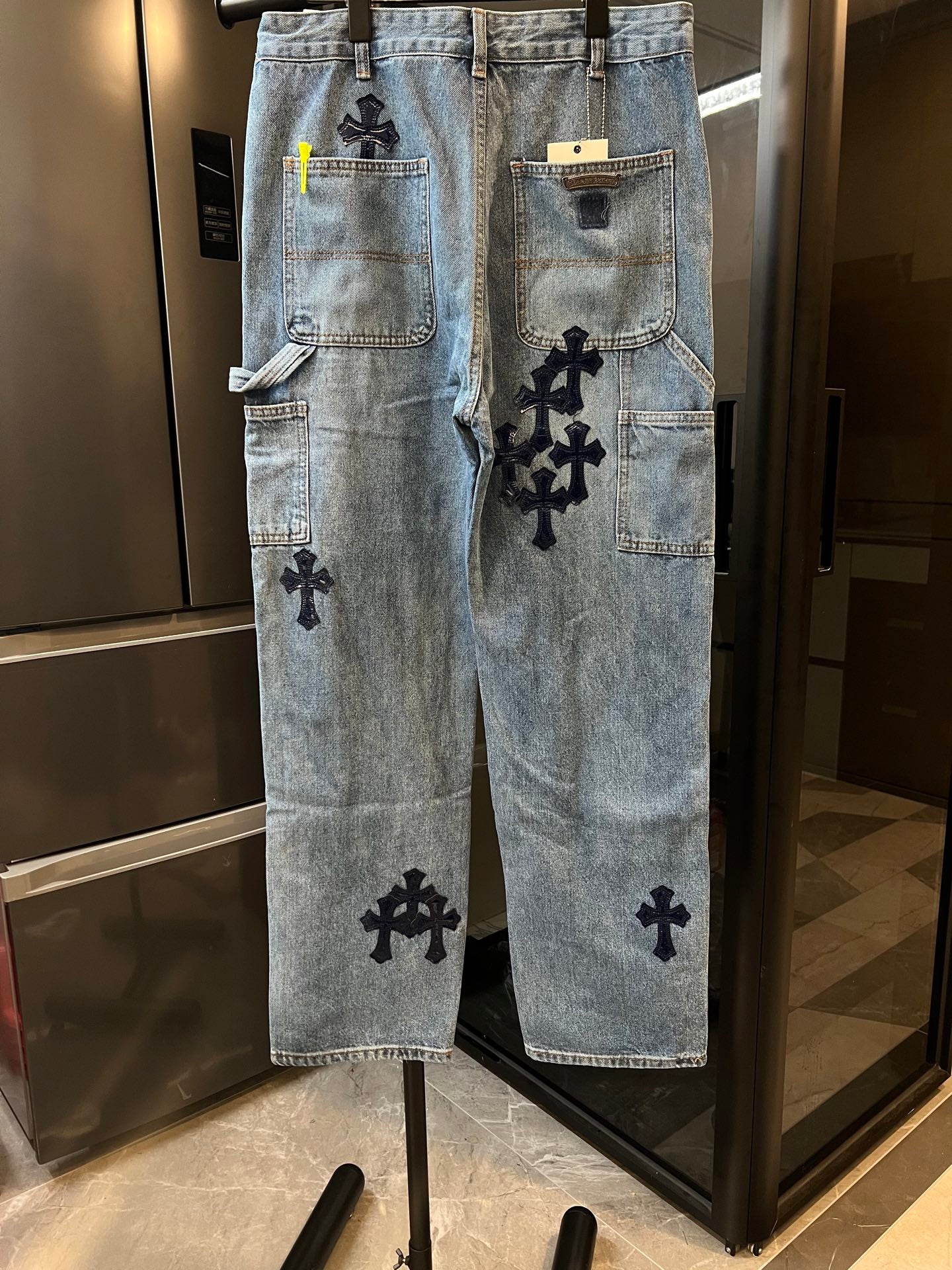 Light-wash denim pants with multiple black cross patches and large side pockets