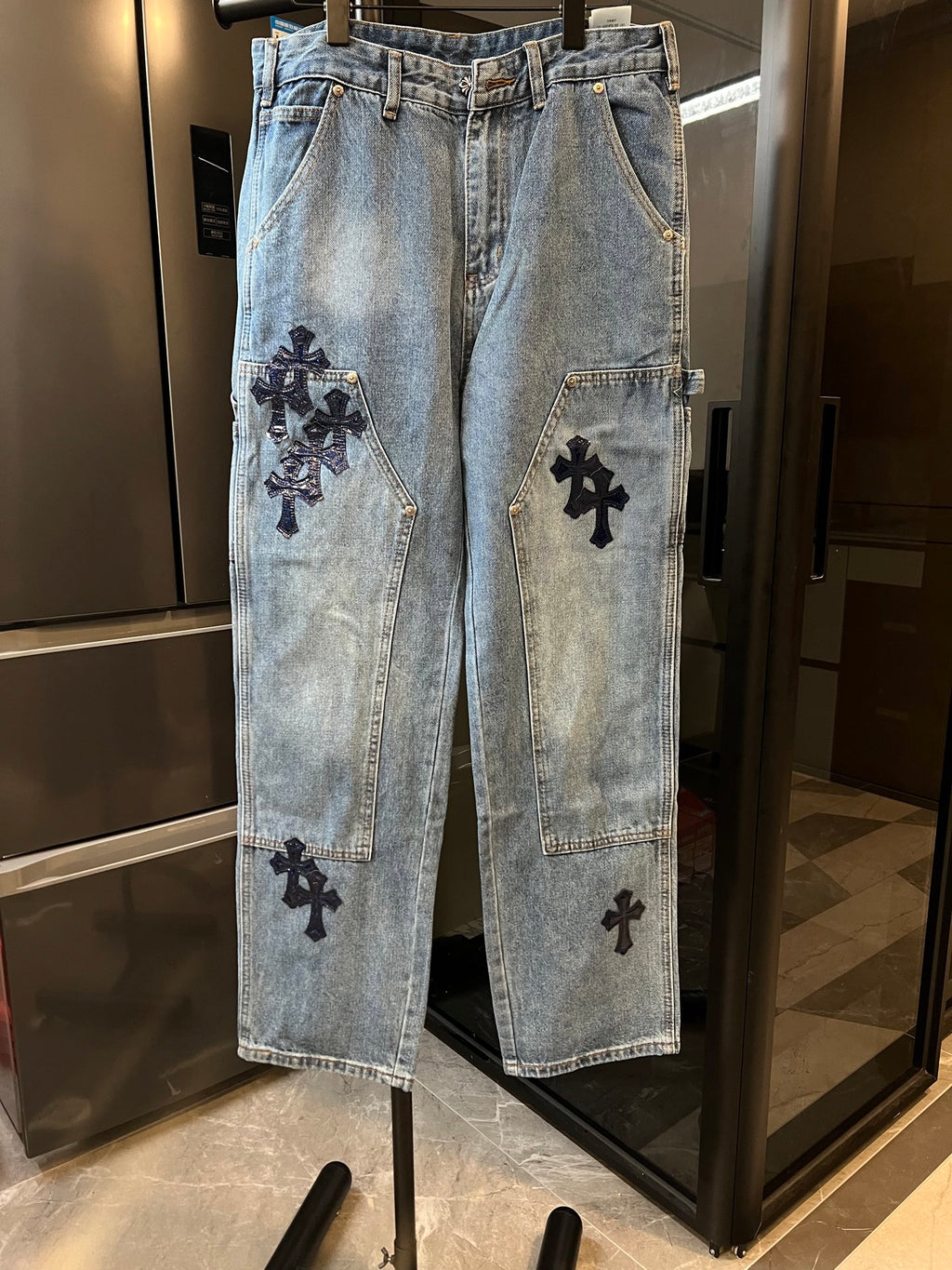 Light-wash denim pants with black cross applique on front leg pockets