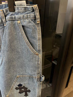 Light-wash denim pants with embroidered black cross patch on thigh