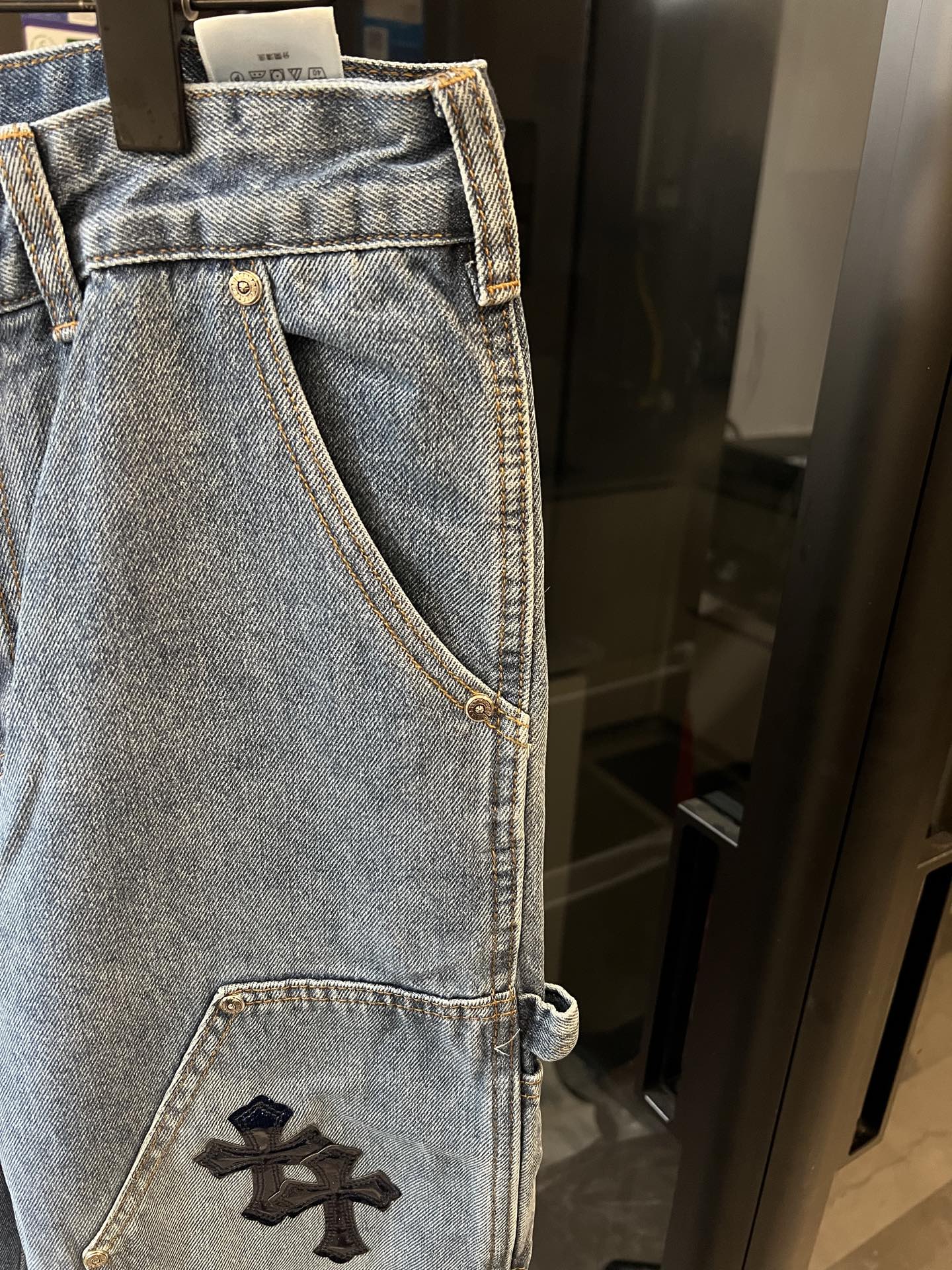 Light-wash denim pants with embroidered black cross patch on thigh