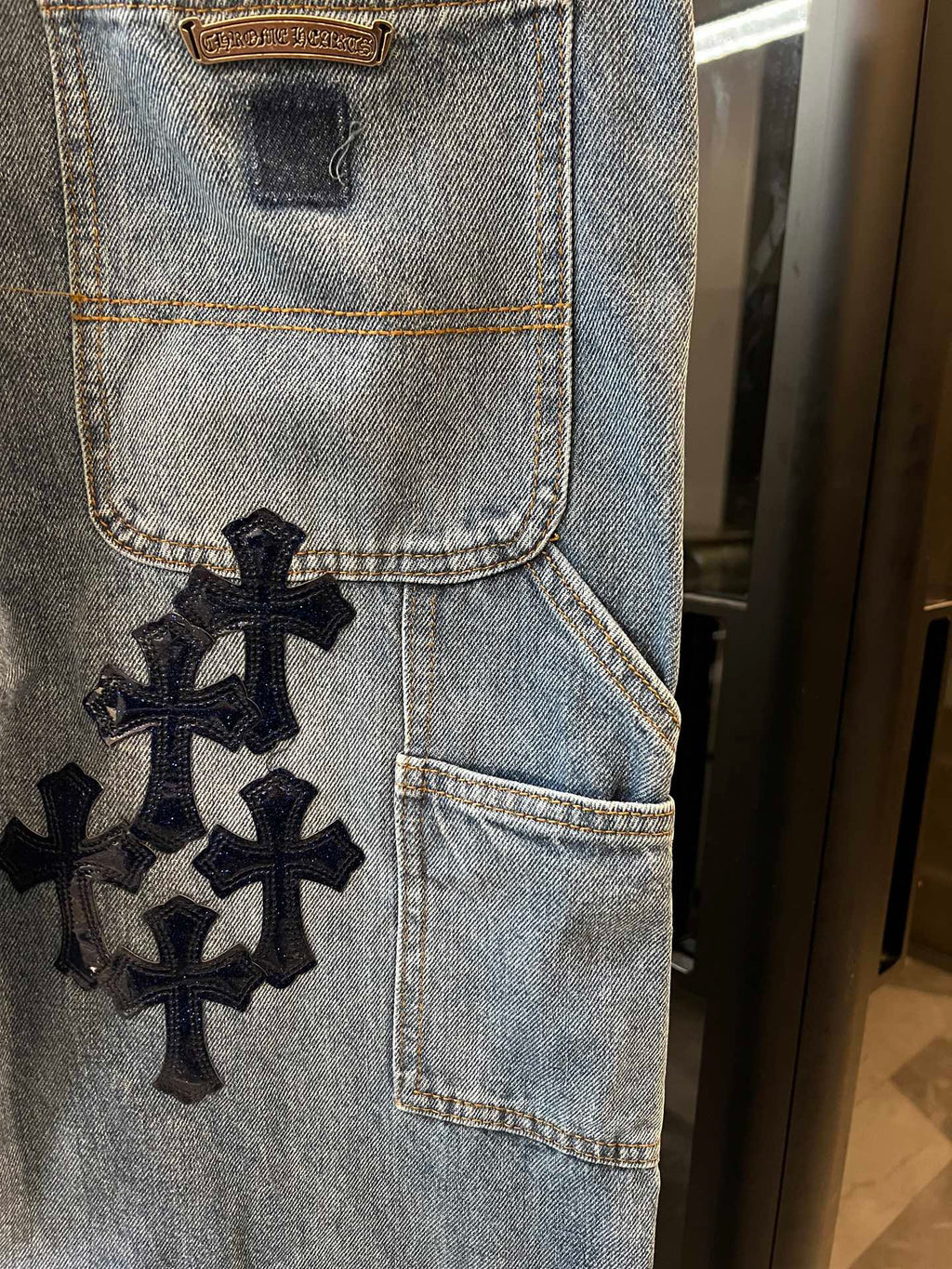 Light-wash denim pocket panel with embroidered black cross patch