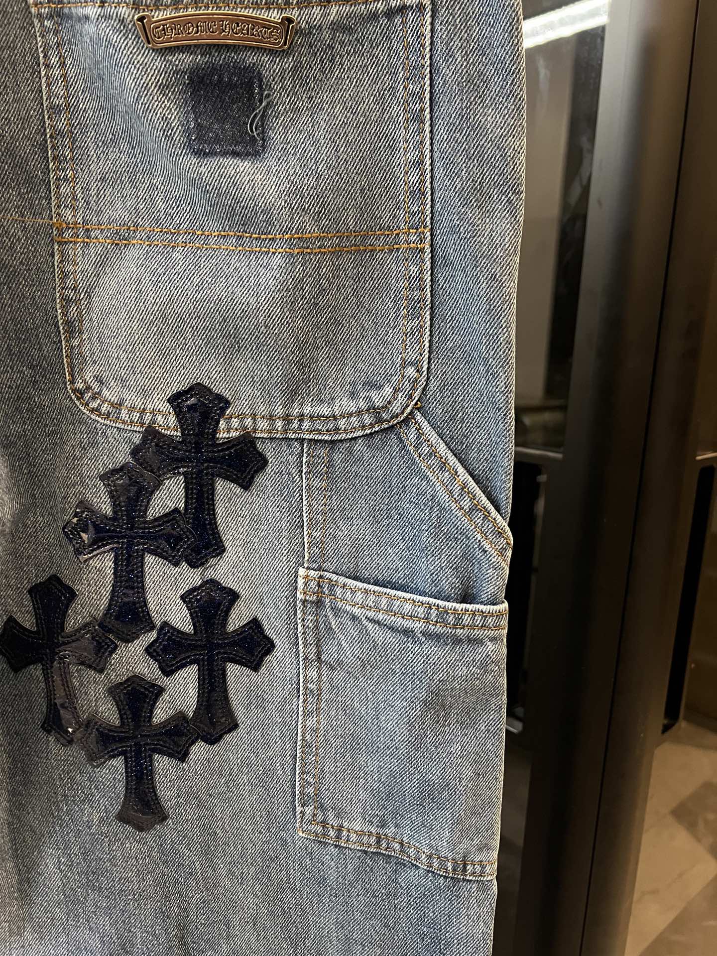 Light-wash denim pocket panel with embroidered black cross patch