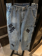 Light-wash denim pants with black cross patches on front pockets and leg panels