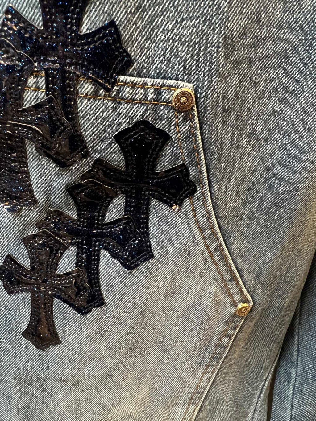 Denim pocket with embroidered black cross pattern and gold-tone button
