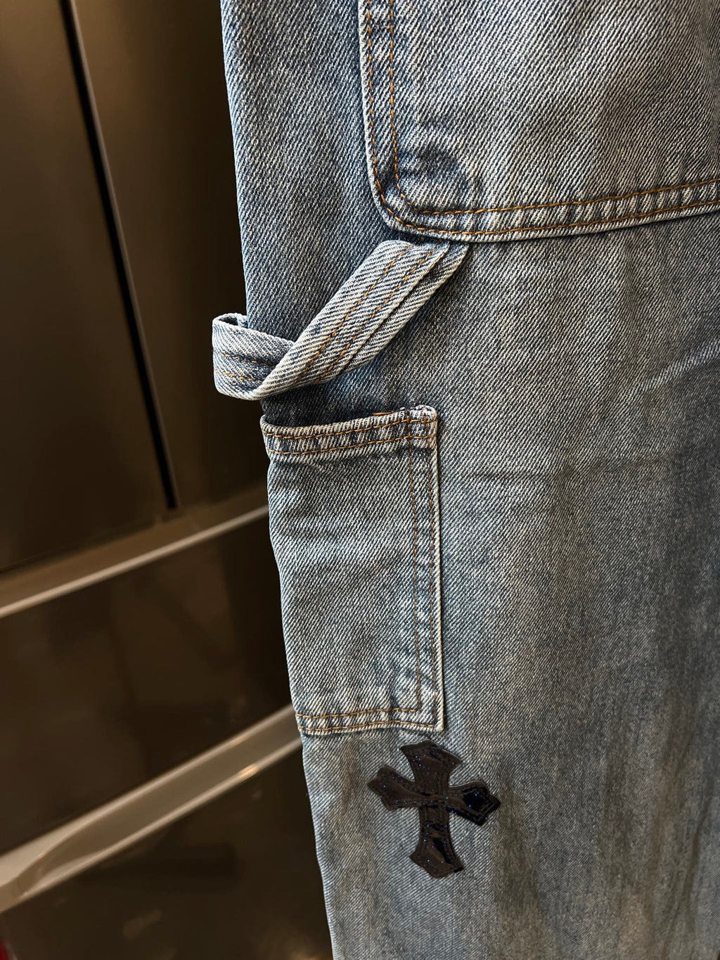 Light-wash denim pant hem with cuff and embroidered black cross patch