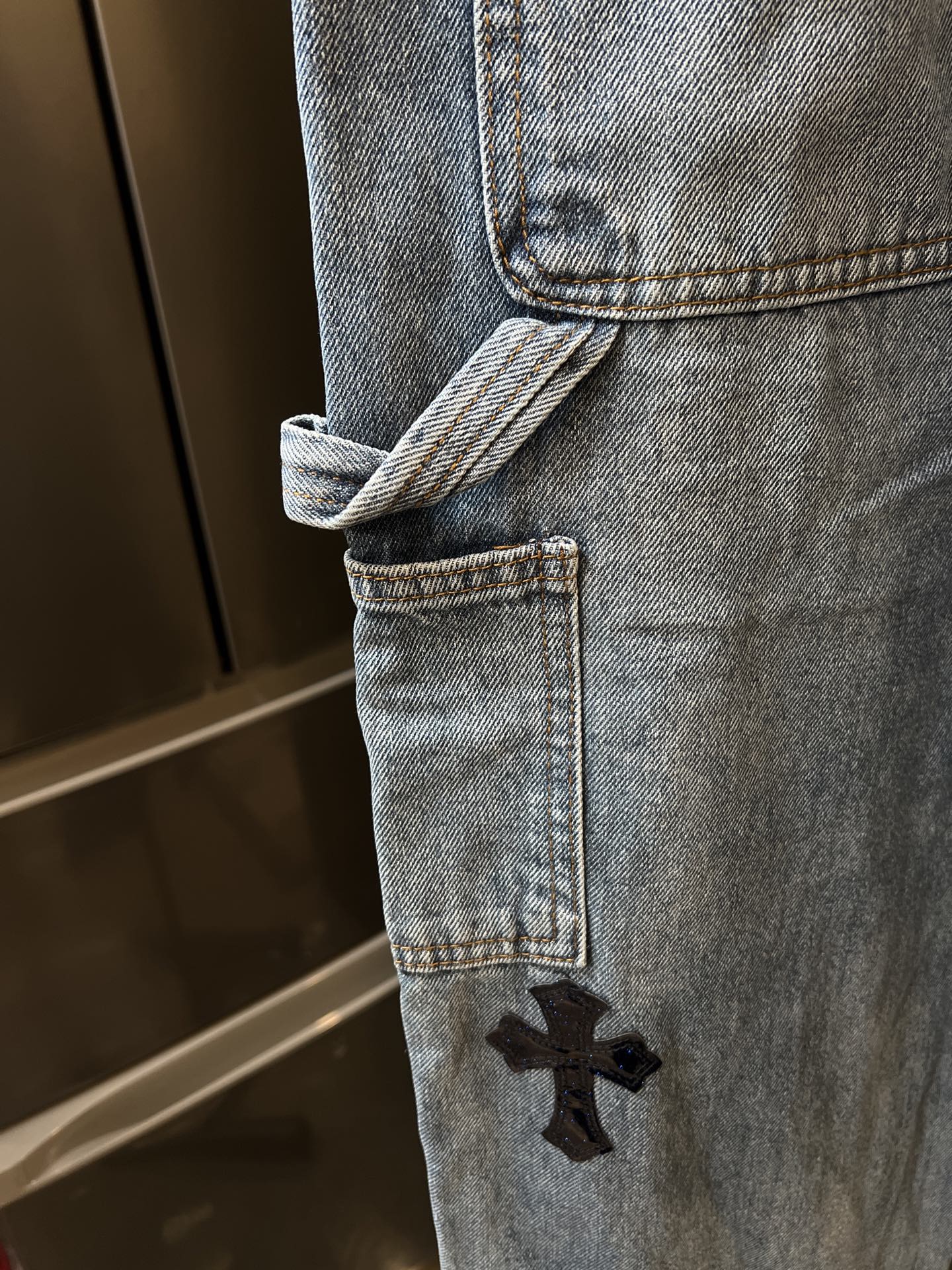 Light-wash denim pant hem with cuff and embroidered black cross patch