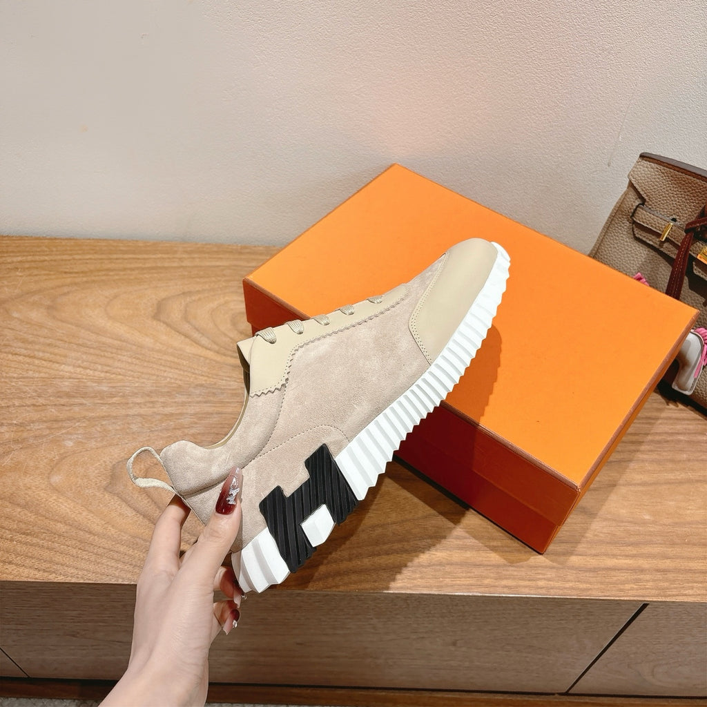 Cream suede sneaker with black-and-white outsole, side view held by hand