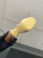 Slingback shoe outsole with gold-toned tread, white upper with red cherry detail.
