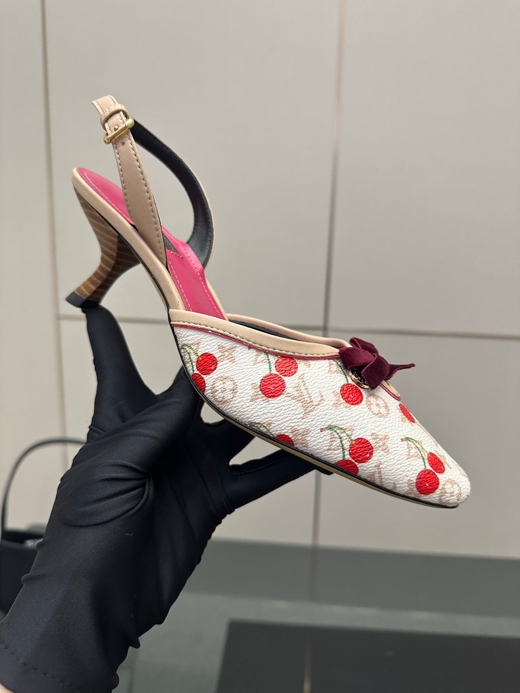 Pointed heeled slingback shoes held in hand, white red cherry print with fuchsia lining.