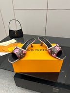 Women's heeled mules with open toe, black floral print, pink bow straps, gold heel