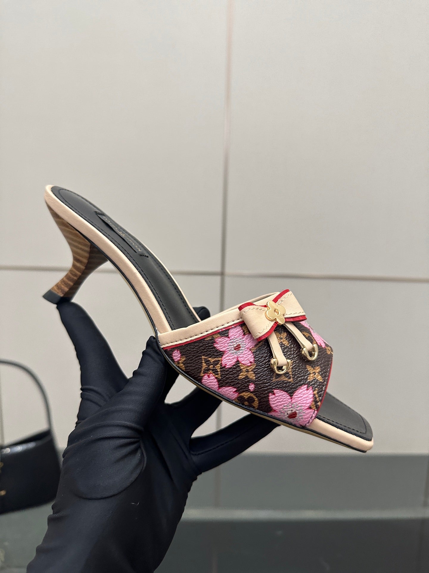 Women's heeled mules, side view: black floral upper with pink bow strap, tan sole