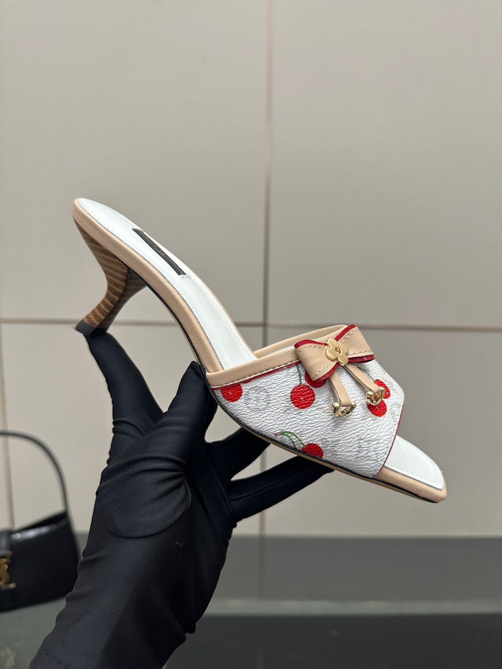 Women’s mules held up: white cherry-print upper with red bow charm and tan heel