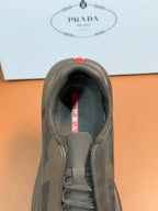 Prada unisex sneaker tongue label, dark gray knit lining with red Prada tab.