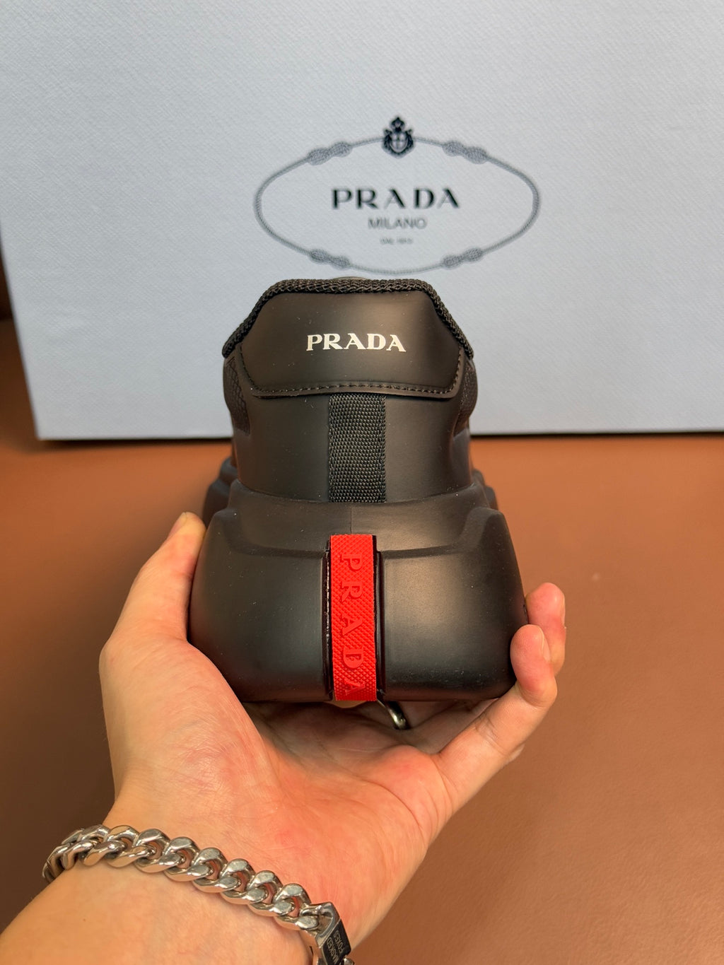 Prada unisex sneaker heel, dark gray with vertical red PRADA strap detail.