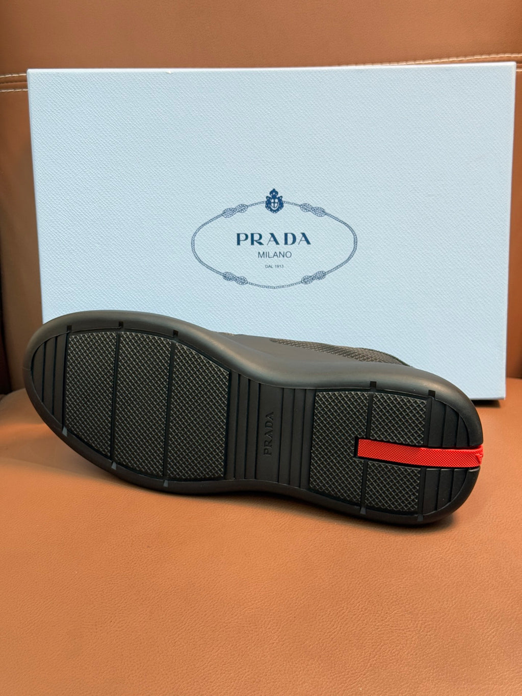 Prada unisex sneakers outsole, dark gray rubber tread with red heel accent.