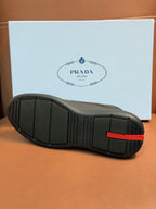 Prada unisex sneakers outsole, dark gray rubber tread with red heel accent.