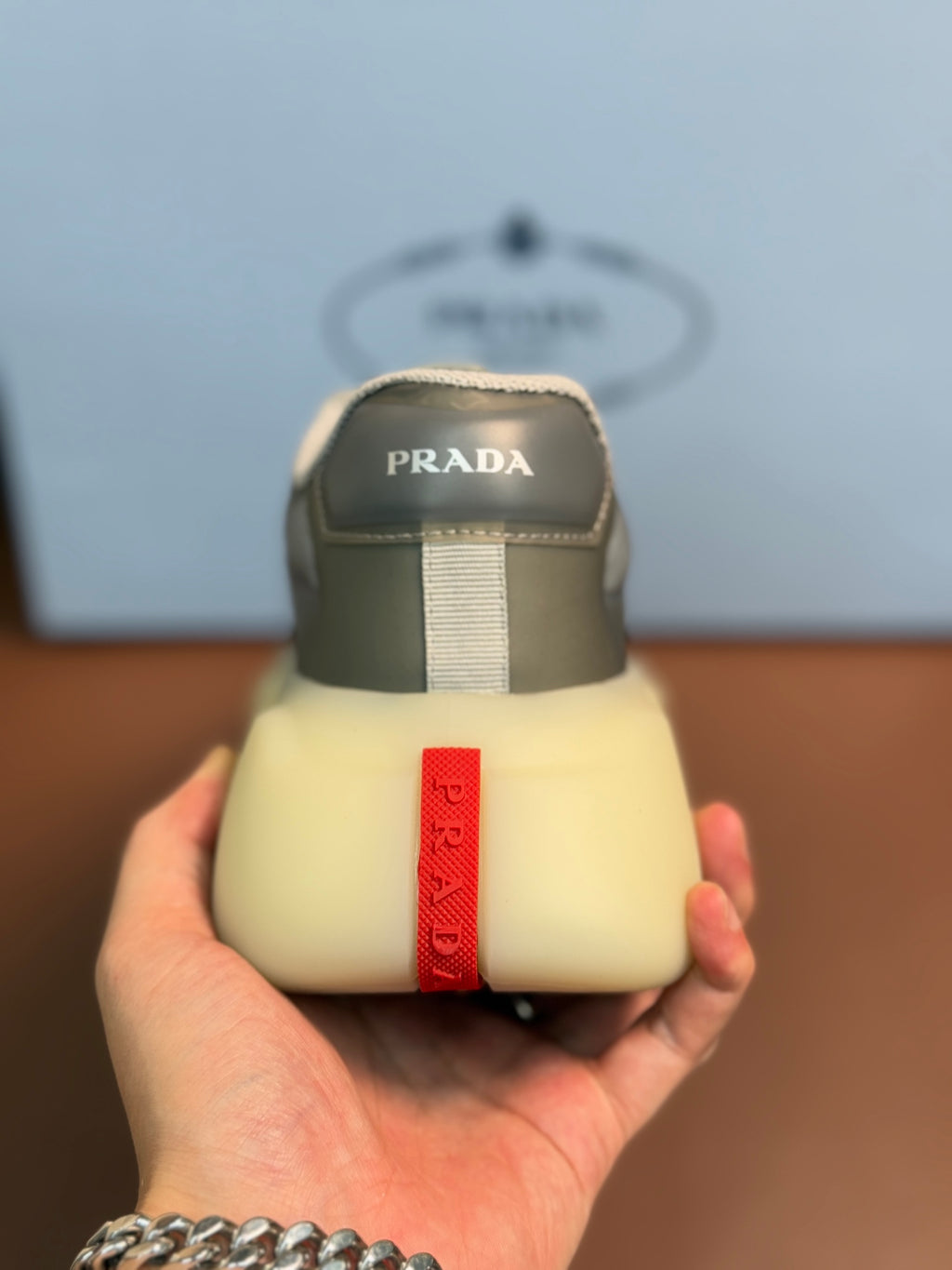 Prada unisex sneakers, heel view with Prada label, cream rubber and gray upper
