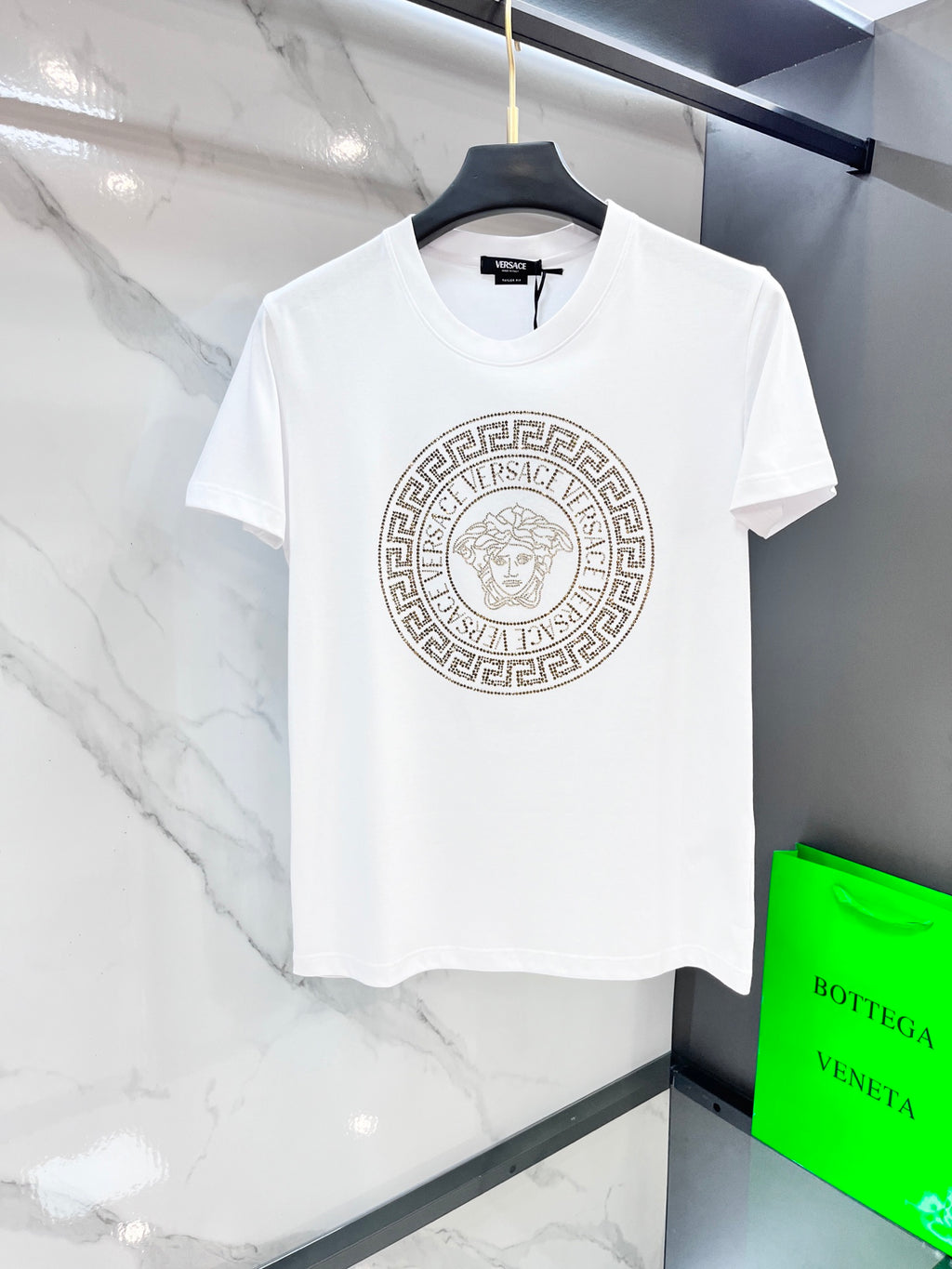 White T-shirt with large gold Medusa-style logo on the front chest