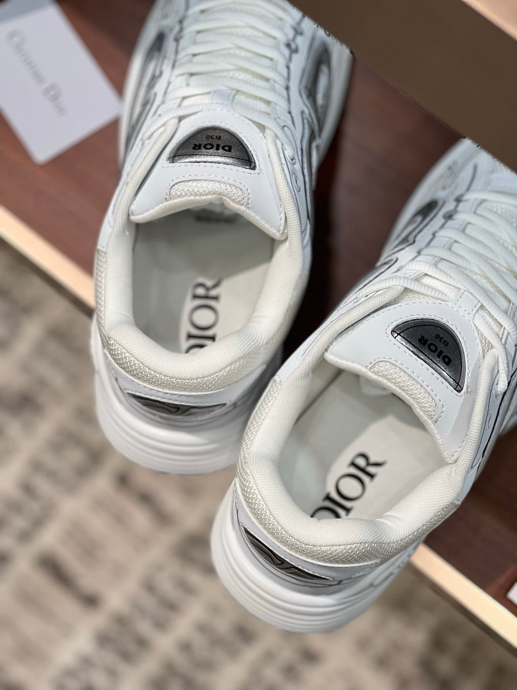 White Dior sneakers with cushioned interior and gray logo patches on tongue and collar
